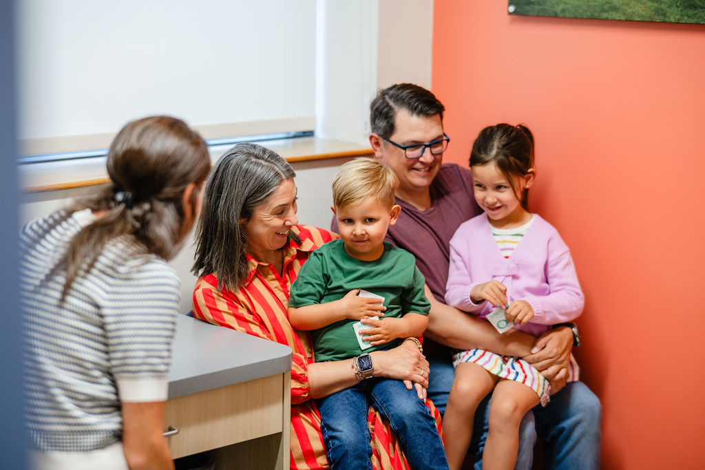a mother and father with their son and daughter sitting on their laps talking to a pediatrician