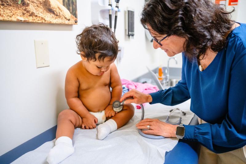 a pediatrician holding a stethoscope against a young boy