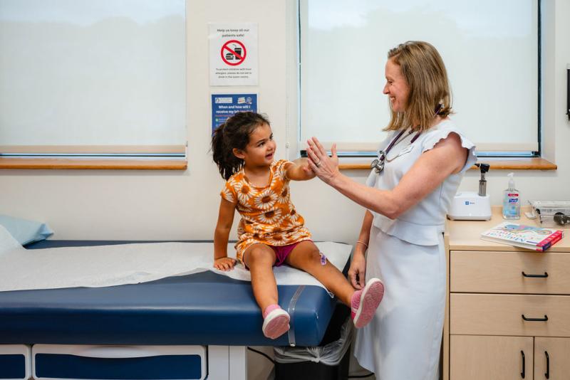 a pediatrician high fiving a young girl on an exam table